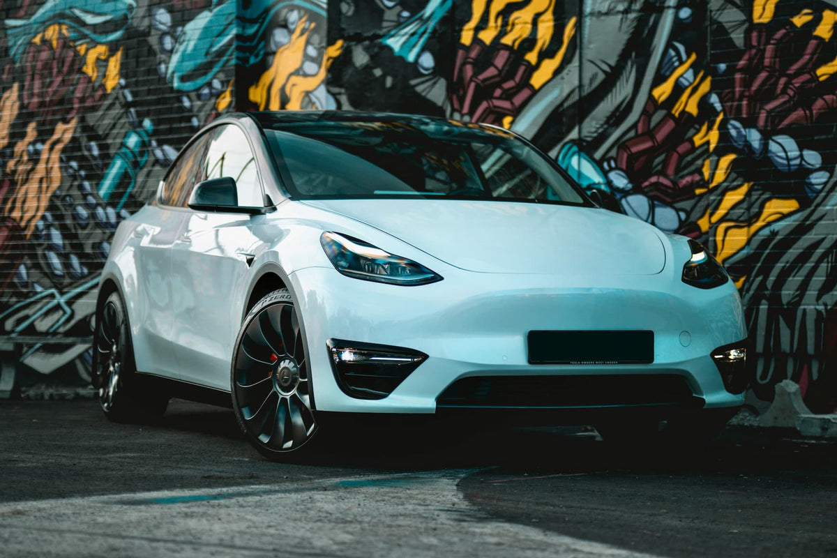 Biala Tesla elektryczna zaparkowana w miejskiej przestrzeni na tle kolorowego graffiti.
