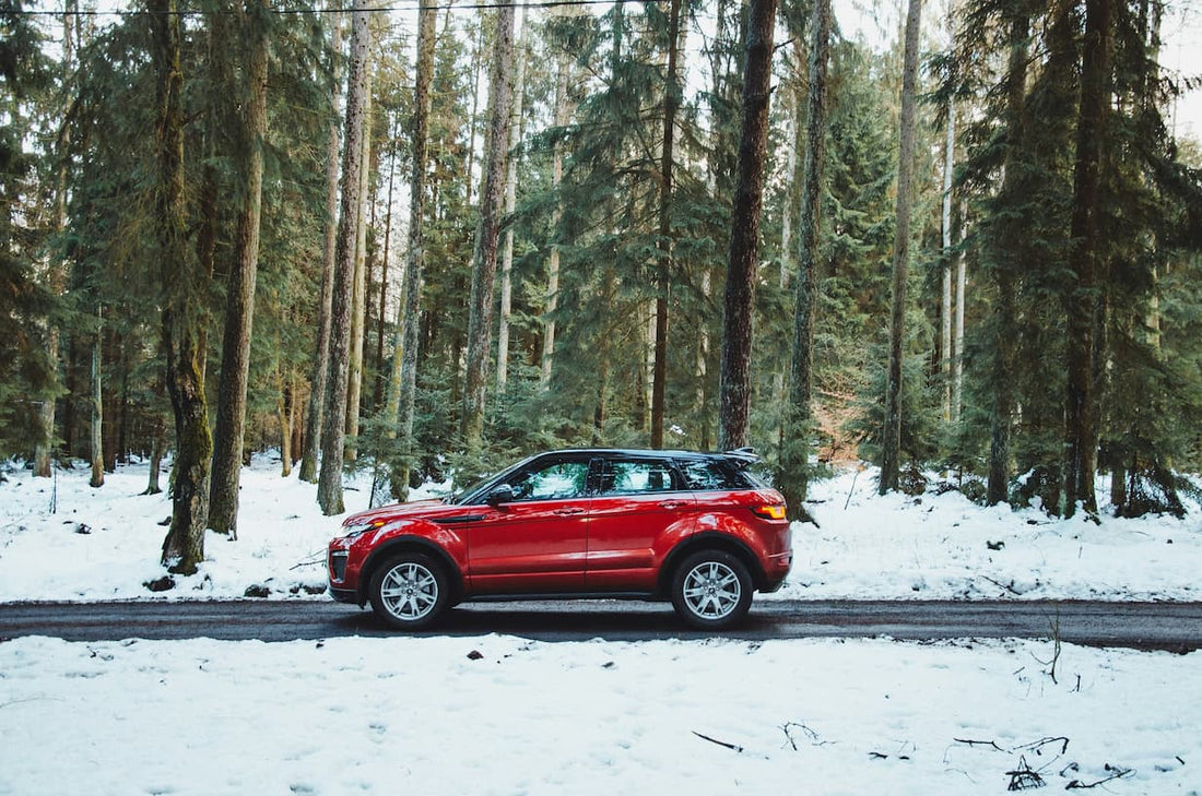 Czerwony SUV zaparkowany na zimowej lesnej drodze wsrod osniezonych drzew.