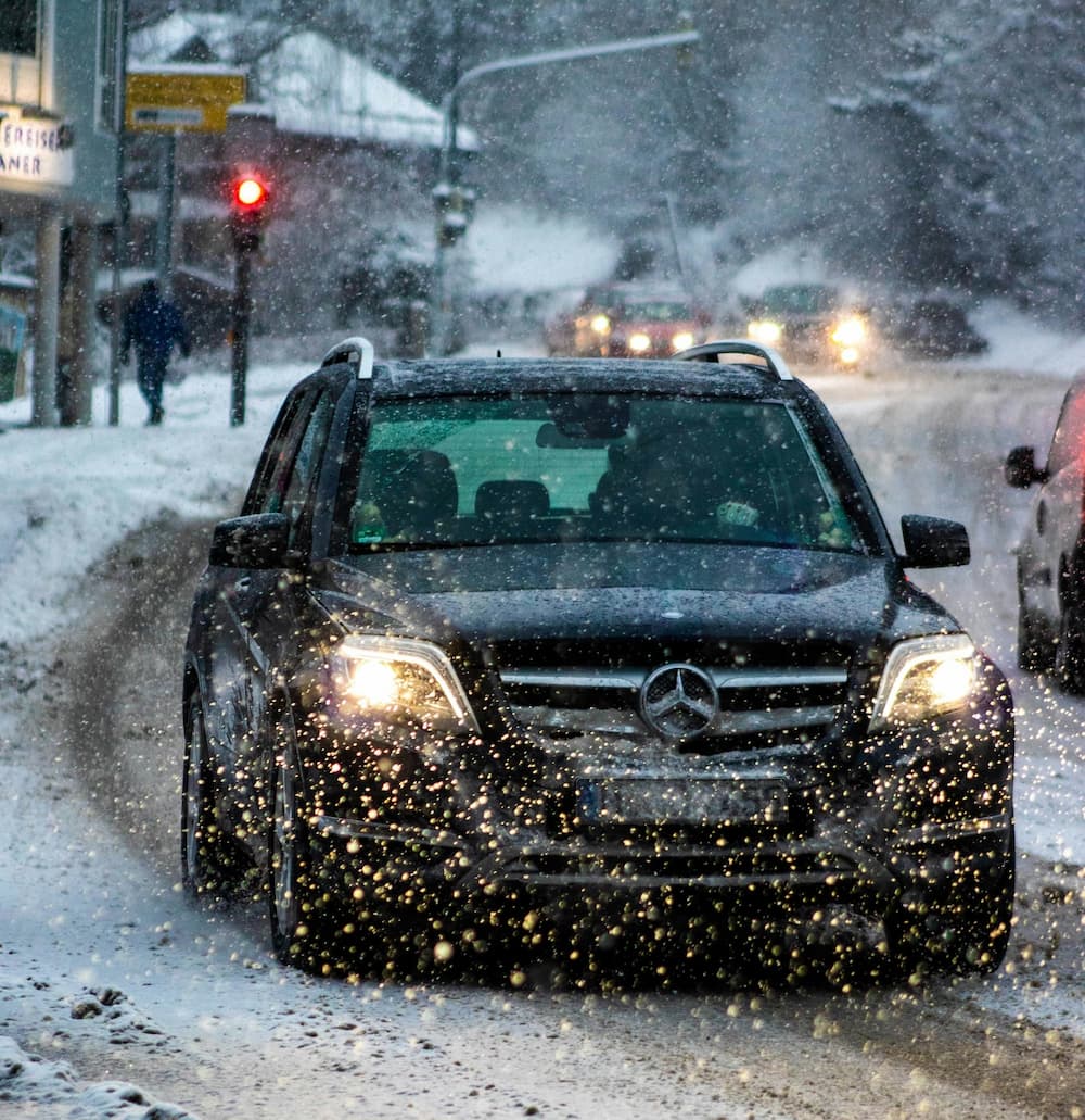 Mercedes SUV jedzie przez mocny opad sniegu po zimowej, zasniezonej drodze z wlaczonymi swiatlami.