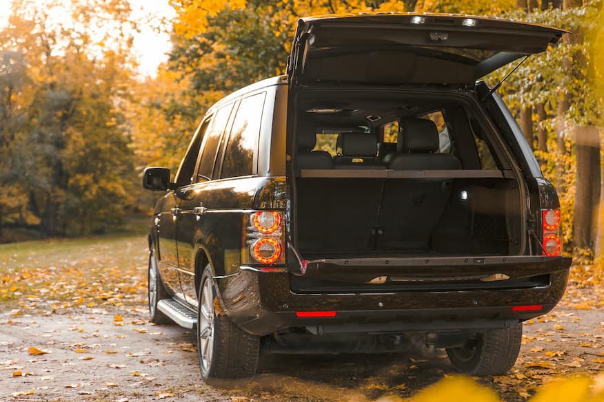 SUV z otwartym bagażnikiem na jesiennej leśnej drodze z liśćmi.