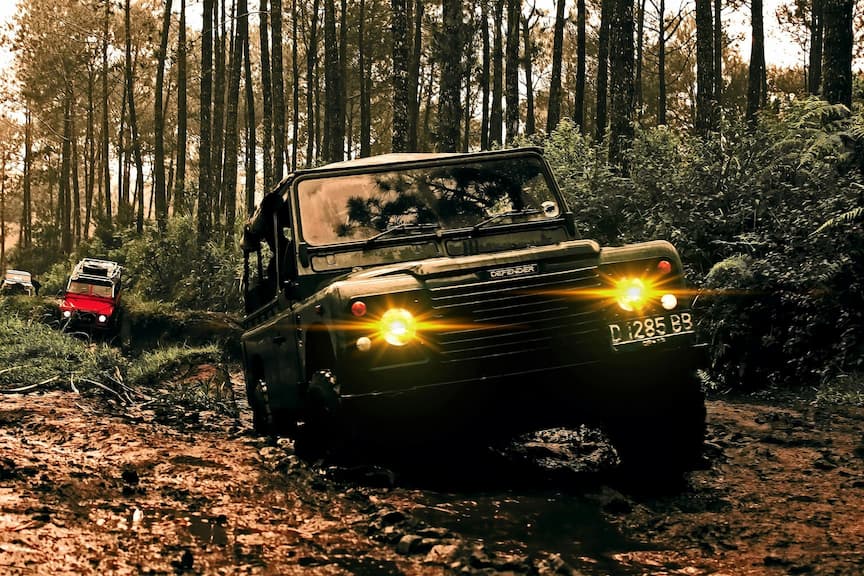 SUV terenowy jedzie przez błotnistą leśną trasę z włączonymi światłami.